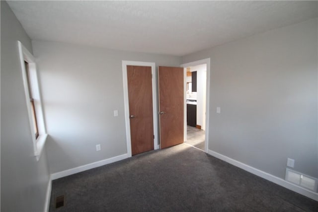 unfurnished bedroom featuring visible vents, dark carpet, and baseboards