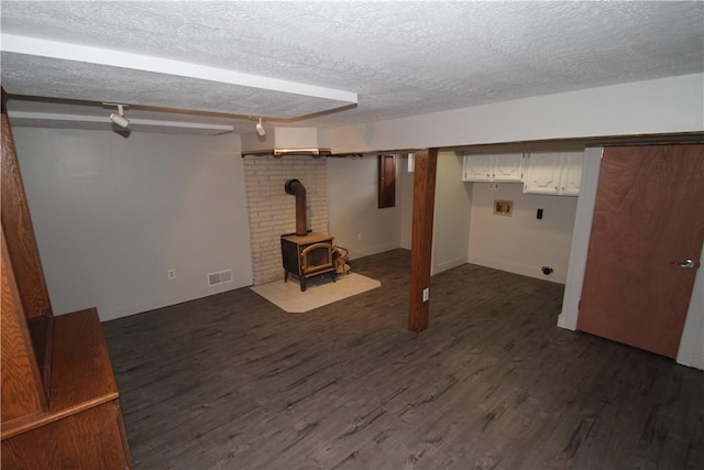 finished below grade area with visible vents, dark wood-type flooring, a textured ceiling, and a wood stove