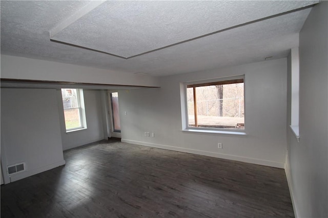 unfurnished room with a textured ceiling, dark wood-style flooring, visible vents, and baseboards