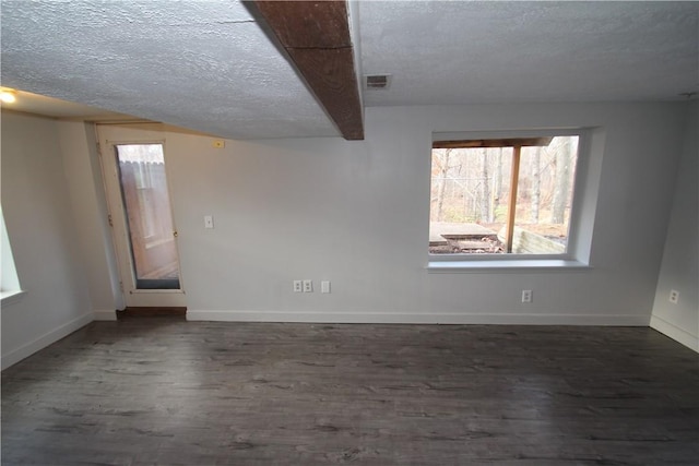 empty room with dark wood-style floors, baseboards, visible vents, and a textured ceiling