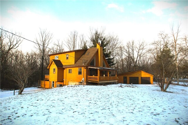 snow covered rear of property with an outdoor structure and a garage