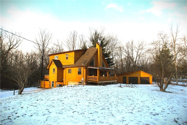 snow covered house with a garage, a chimney, and an outbuilding