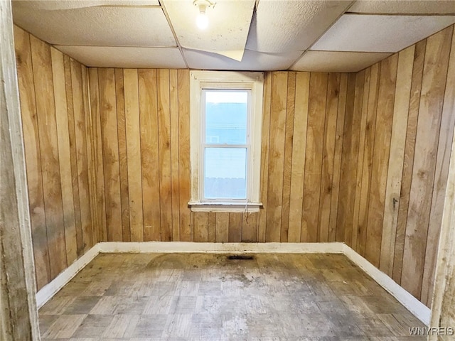 spare room featuring wood-type flooring, a paneled ceiling, and wood walls