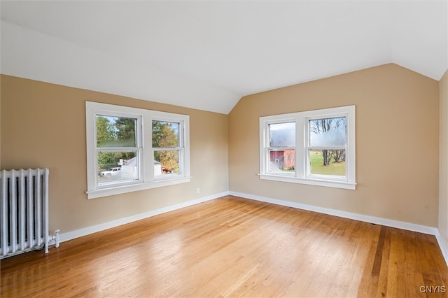 additional living space with radiator heating unit, light hardwood / wood-style floors, and vaulted ceiling