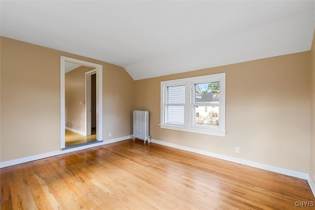 unfurnished room with radiator, vaulted ceiling, and light wood-type flooring