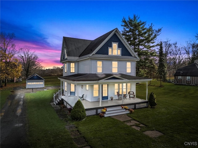 back house at dusk with covered porch, a lawn, a garage, and an outdoor structure