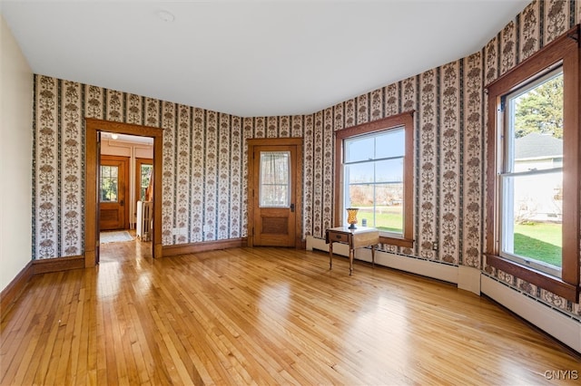 unfurnished room with baseboard heating, plenty of natural light, and light wood-type flooring