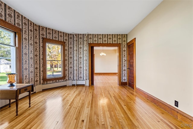 empty room with light hardwood / wood-style flooring, a wealth of natural light, and a chandelier