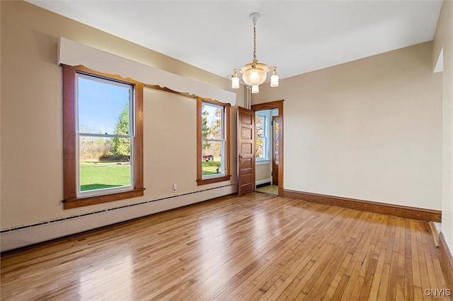 empty room featuring baseboard heating, a notable chandelier, wood-type flooring, and a healthy amount of sunlight