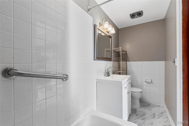 bathroom featuring vanity, toilet, and tile walls