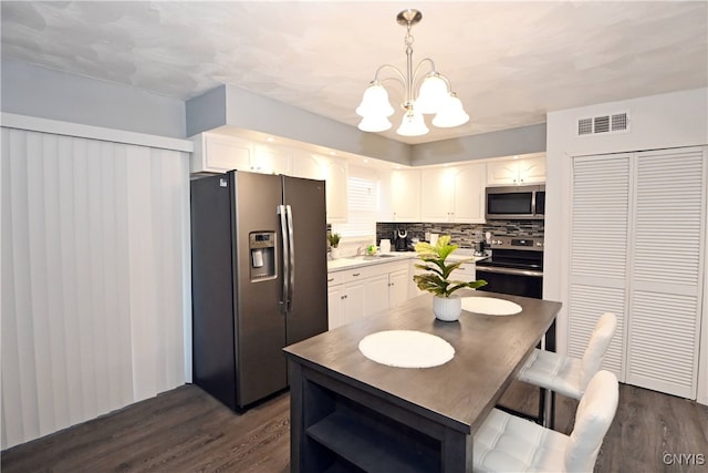 kitchen featuring white cabinetry, stainless steel appliances, dark hardwood / wood-style floors, backsplash, and decorative light fixtures