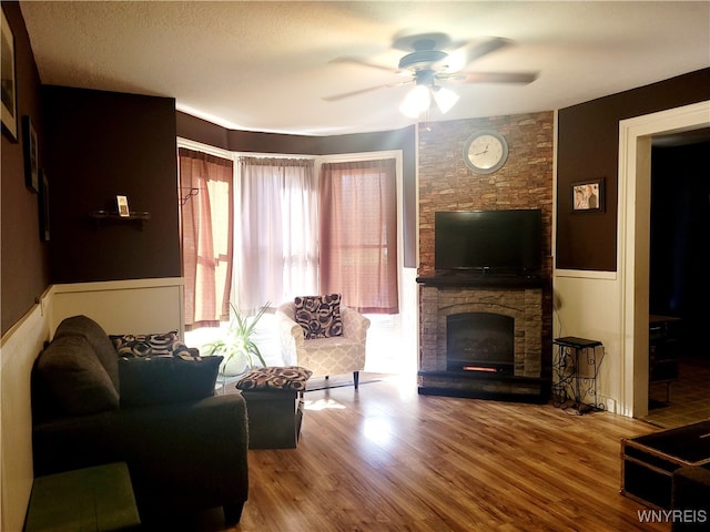 living room featuring hardwood / wood-style floors, ceiling fan, a fireplace, and a textured ceiling