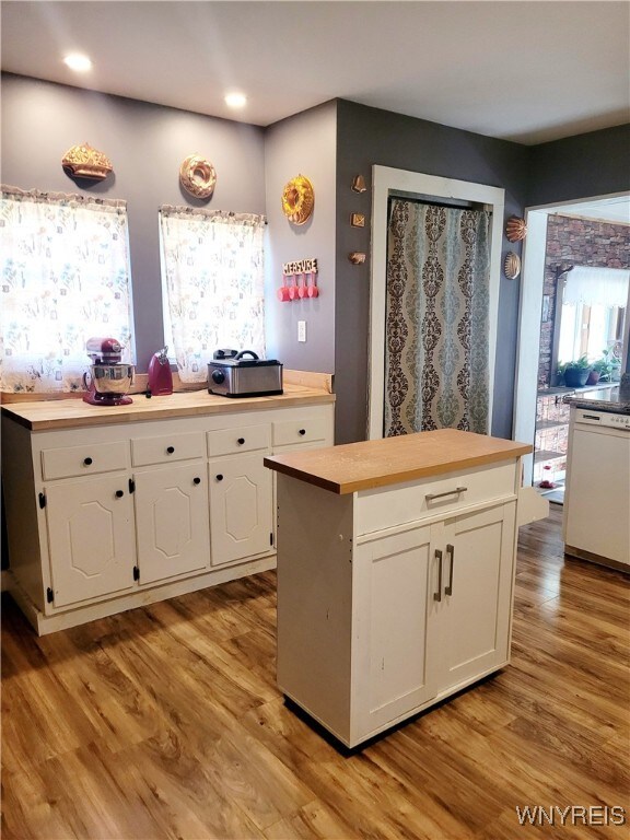 kitchen with white dishwasher, a kitchen island, white cabinetry, and light hardwood / wood-style flooring