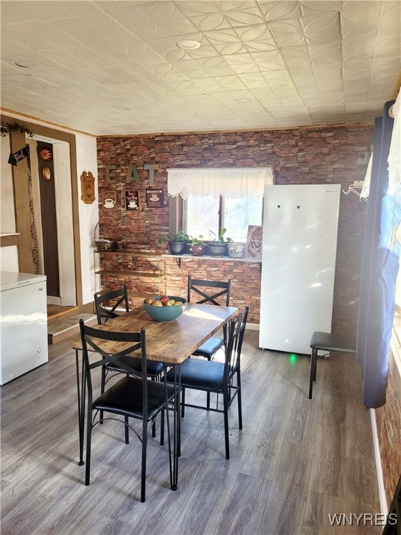 dining area with brick wall and hardwood / wood-style flooring