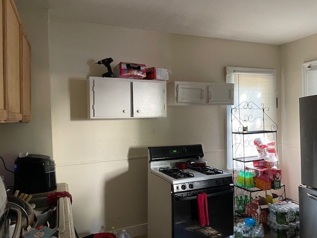 kitchen with white cabinets, stainless steel refrigerator, and white range with gas cooktop