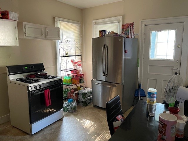 kitchen with stainless steel fridge, white range with gas stovetop, and white cabinetry