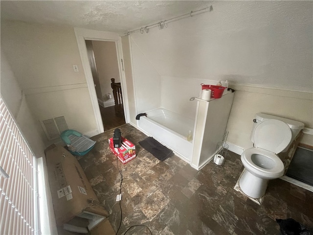 bathroom with a bathtub, toilet, and a textured ceiling