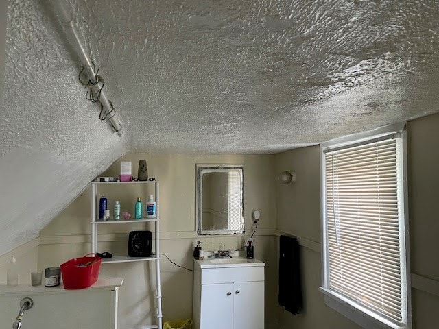 bathroom with rail lighting, vanity, lofted ceiling, and a textured ceiling