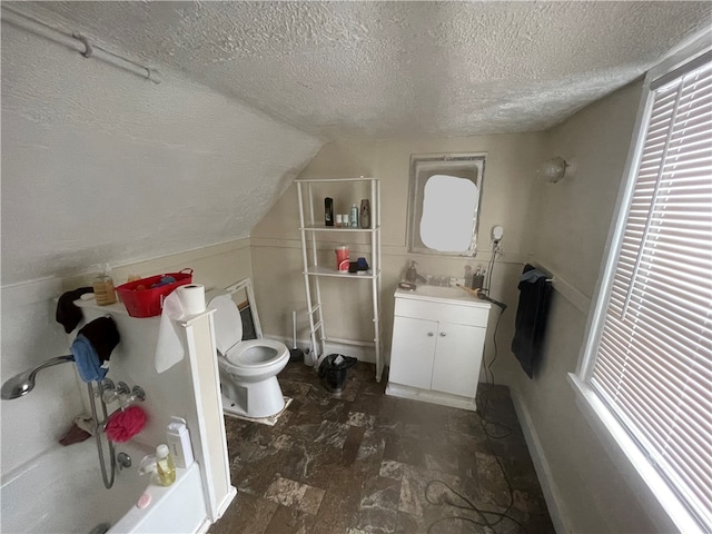 bathroom with vanity, a bathtub, vaulted ceiling, toilet, and a textured ceiling