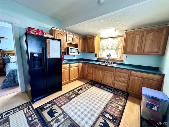 kitchen with black refrigerator with ice dispenser, sink, light hardwood / wood-style floors, and a textured ceiling