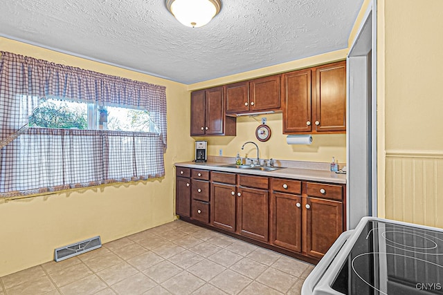 kitchen featuring a textured ceiling, light tile patterned flooring, range, and sink