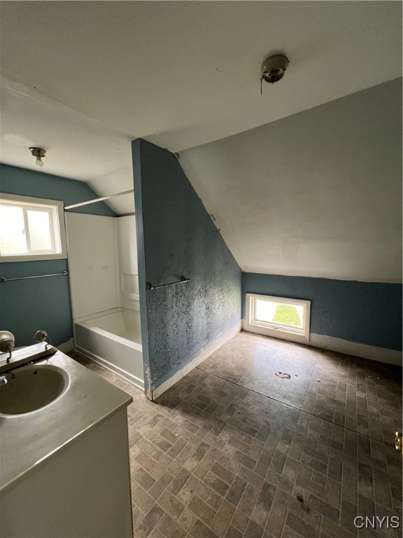 bathroom with vanity, vaulted ceiling, a wealth of natural light, and tub / shower combination