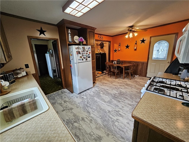 kitchen with wood walls, white appliances, sink, ornamental molding, and dark brown cabinets