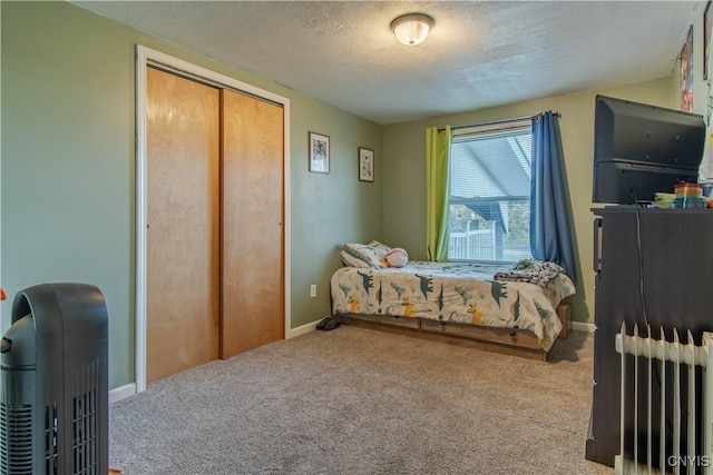 bedroom featuring radiator heating unit, a textured ceiling, light colored carpet, and a closet