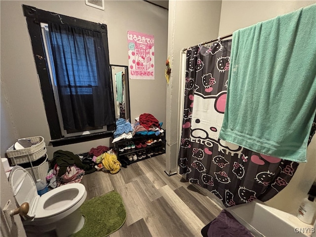 bathroom featuring toilet, hardwood / wood-style floors, and shower / tub combo with curtain