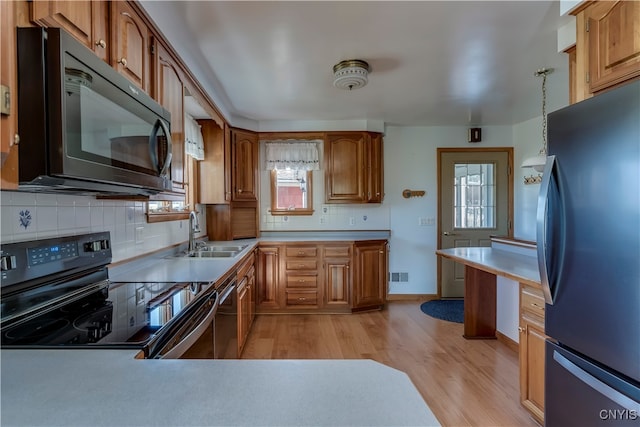 kitchen featuring pendant lighting, stainless steel refrigerator, black electric range oven, sink, and light hardwood / wood-style floors