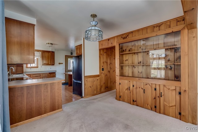 kitchen with pendant lighting, wooden walls, sink, light colored carpet, and black fridge