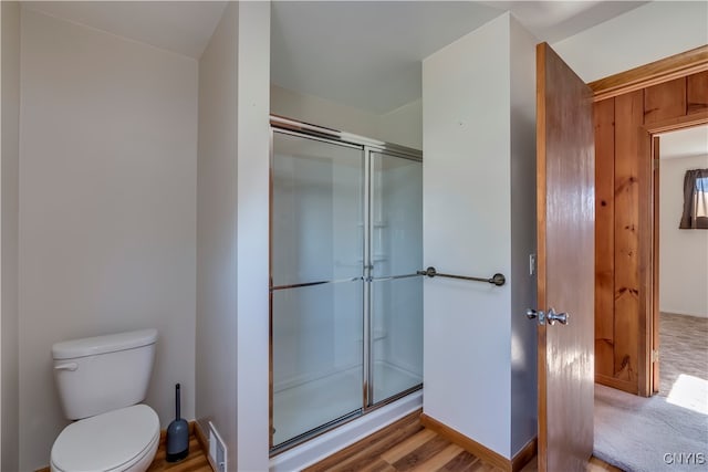 bathroom with wood-type flooring, a shower with shower door, and toilet