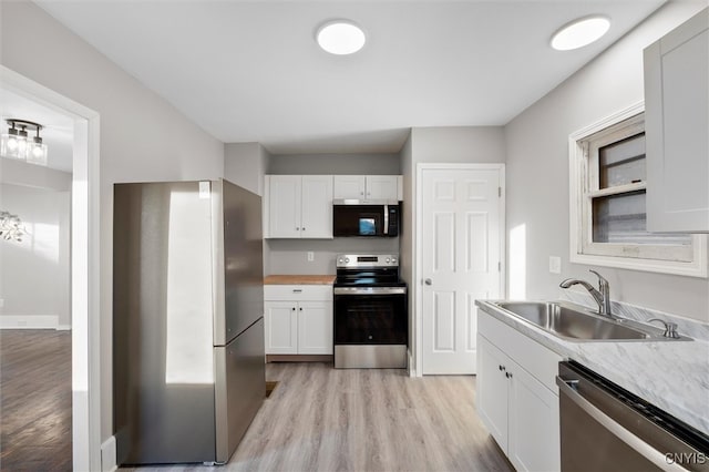 kitchen with appliances with stainless steel finishes, light hardwood / wood-style flooring, white cabinetry, and sink