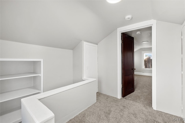 hallway with light colored carpet and lofted ceiling