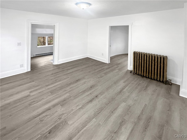 empty room with light hardwood / wood-style flooring, radiator, and a baseboard heating unit