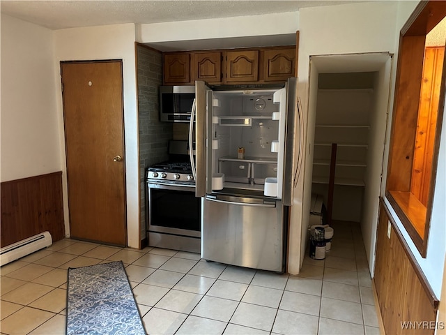 kitchen featuring wooden walls, light tile patterned floors, baseboard heating, and appliances with stainless steel finishes