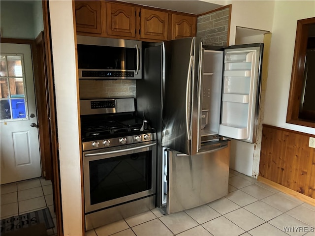 kitchen featuring decorative backsplash, light tile patterned flooring, stainless steel appliances, and wooden walls