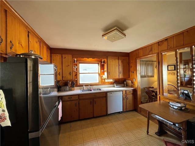 kitchen with stainless steel refrigerator, wooden walls, dishwasher, and sink