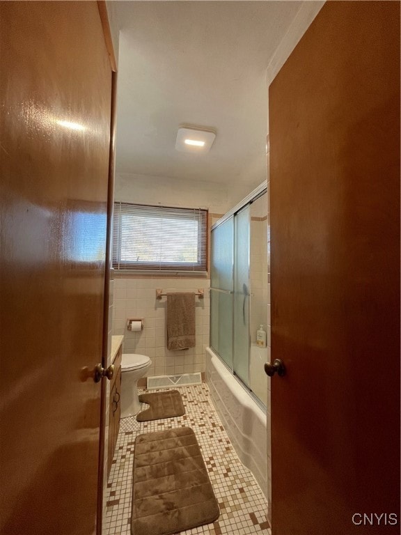 bathroom with tile patterned flooring, toilet, combined bath / shower with glass door, and tile walls