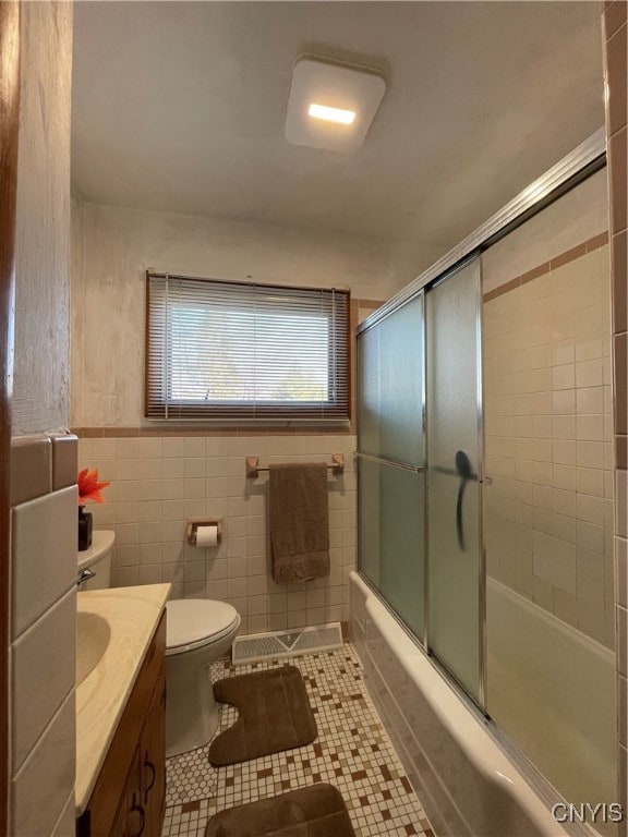 full bathroom featuring tile patterned flooring, combined bath / shower with glass door, toilet, vanity, and tile walls