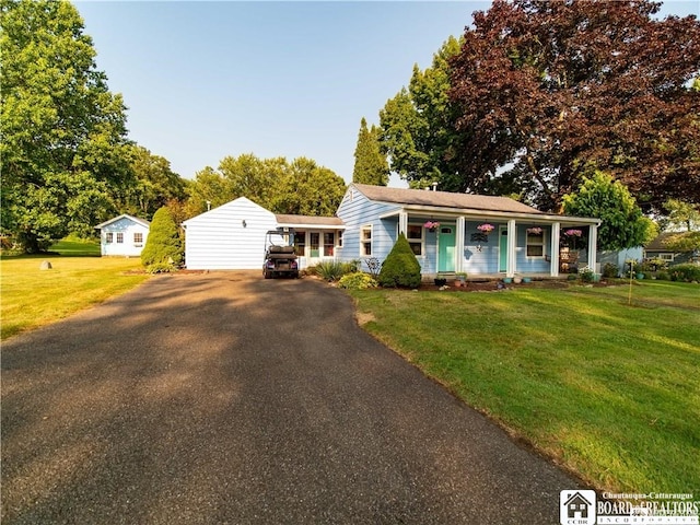 view of front facade featuring an outbuilding, covered porch, a front yard, and a garage