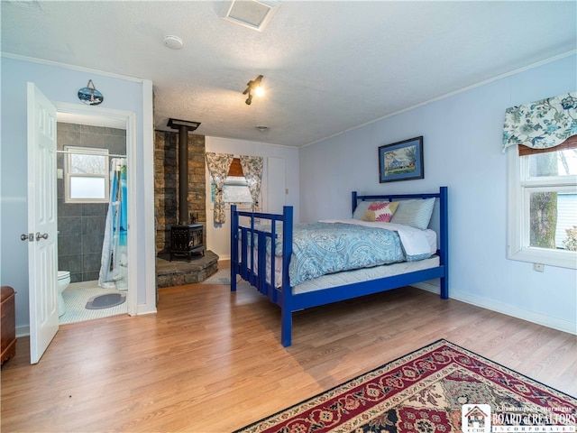bedroom featuring wood-type flooring, a textured ceiling, a wood stove, and crown molding