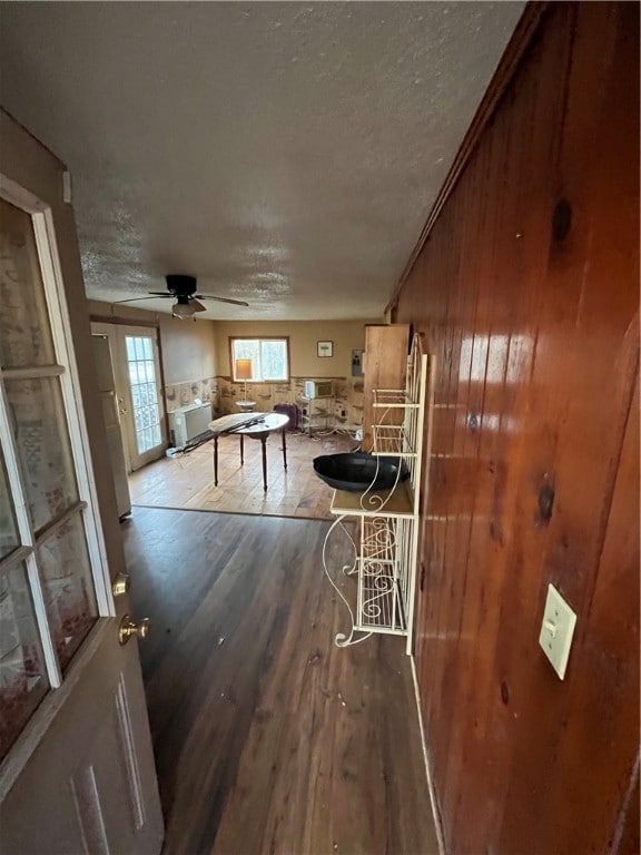 interior space with ceiling fan, crown molding, wood-type flooring, a textured ceiling, and wooden walls