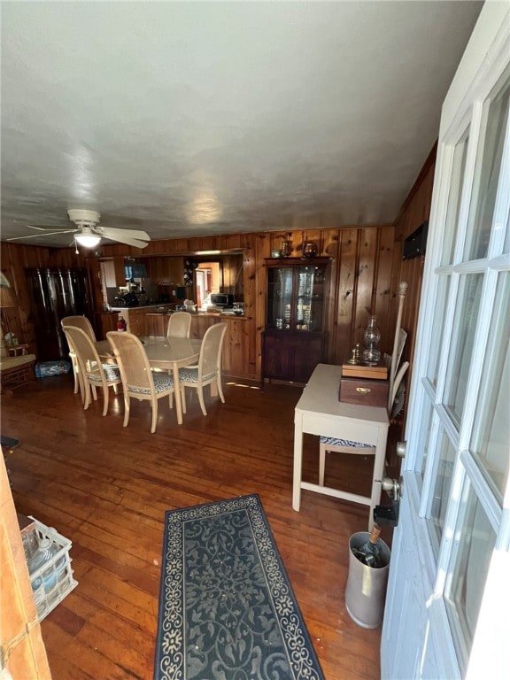 dining room with dark hardwood / wood-style floors, ceiling fan, and wood walls