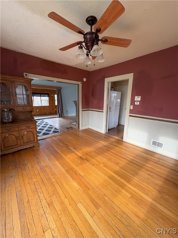 unfurnished living room with ceiling fan, light hardwood / wood-style floors, and a textured ceiling