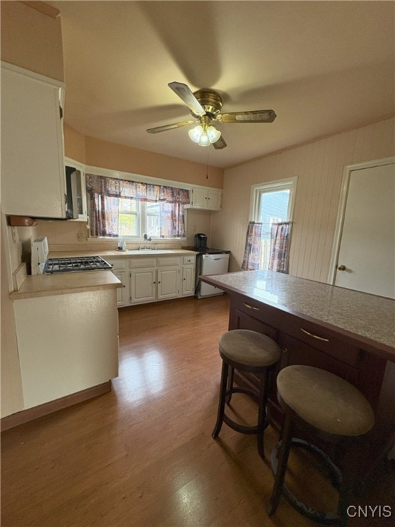 kitchen with ceiling fan, sink, wood-type flooring, stainless steel range oven, and white cabinetry