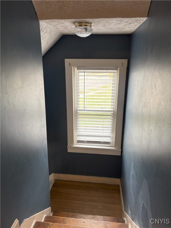 staircase with wood-type flooring, a textured ceiling, and vaulted ceiling