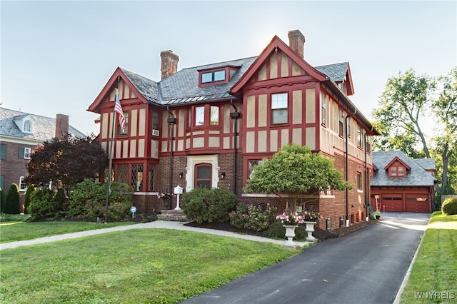 tudor-style house with an outbuilding, a front lawn, and a garage