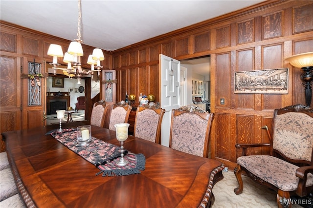 dining area with wood walls, crown molding, and an inviting chandelier