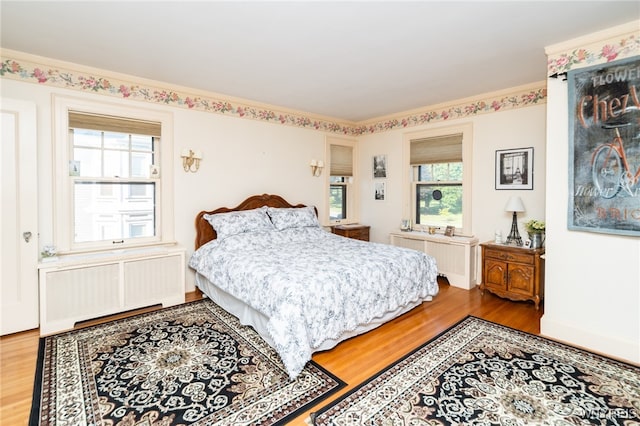 bedroom with wood-type flooring, radiator heating unit, and multiple windows